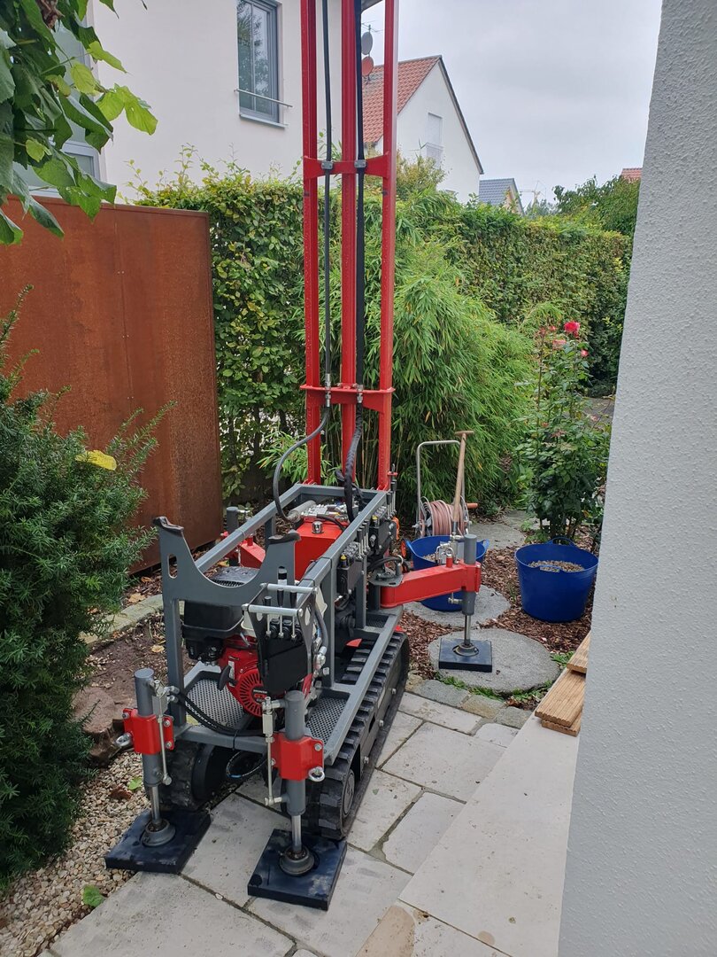 Kompaktes rotes Bohrgerät in einem schmalen Gartenzugang
